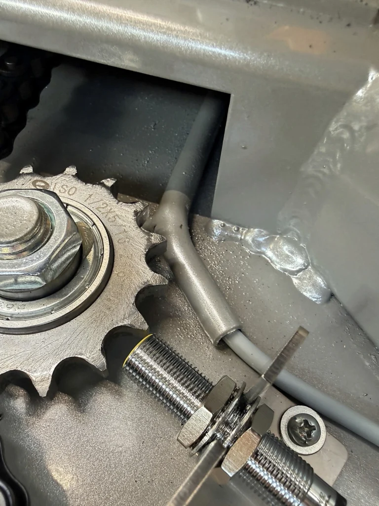 Metal cable protection beside a chain sprocket in the POLPACK ZEUS Wrapper base