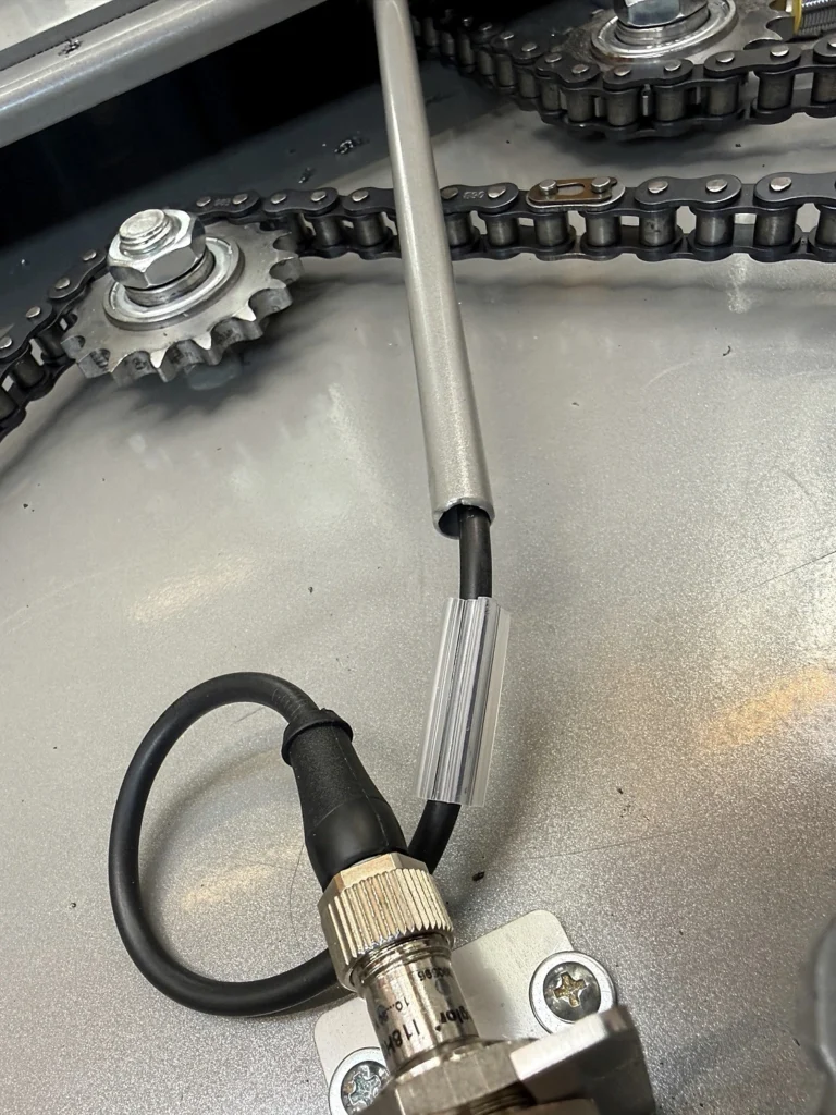 Sensor cable routed through a metal protective tube in the POLPACK ZEUS wrapper base